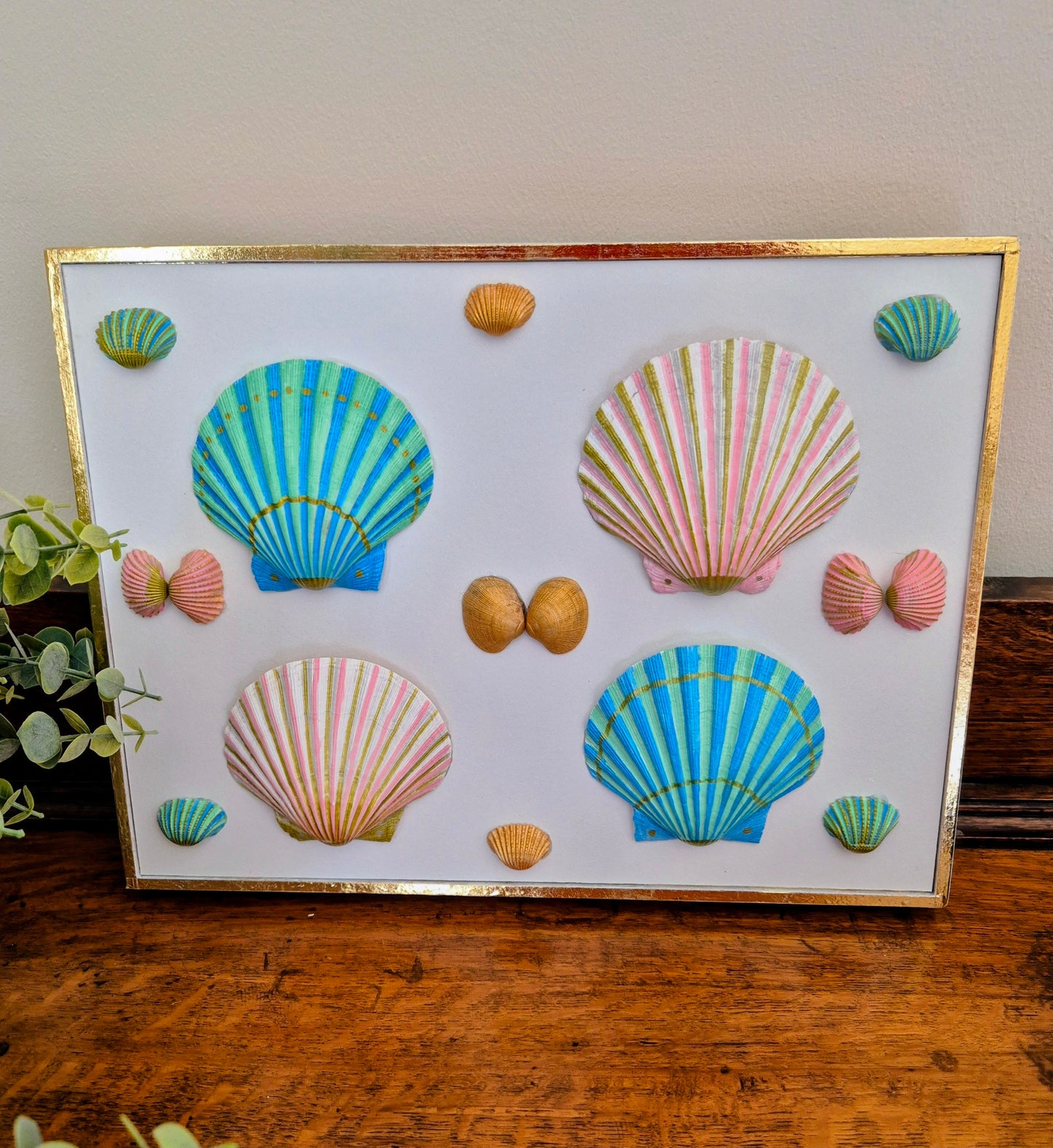 Decorative wall art with colorful shell designs on a white background, framed in gold.