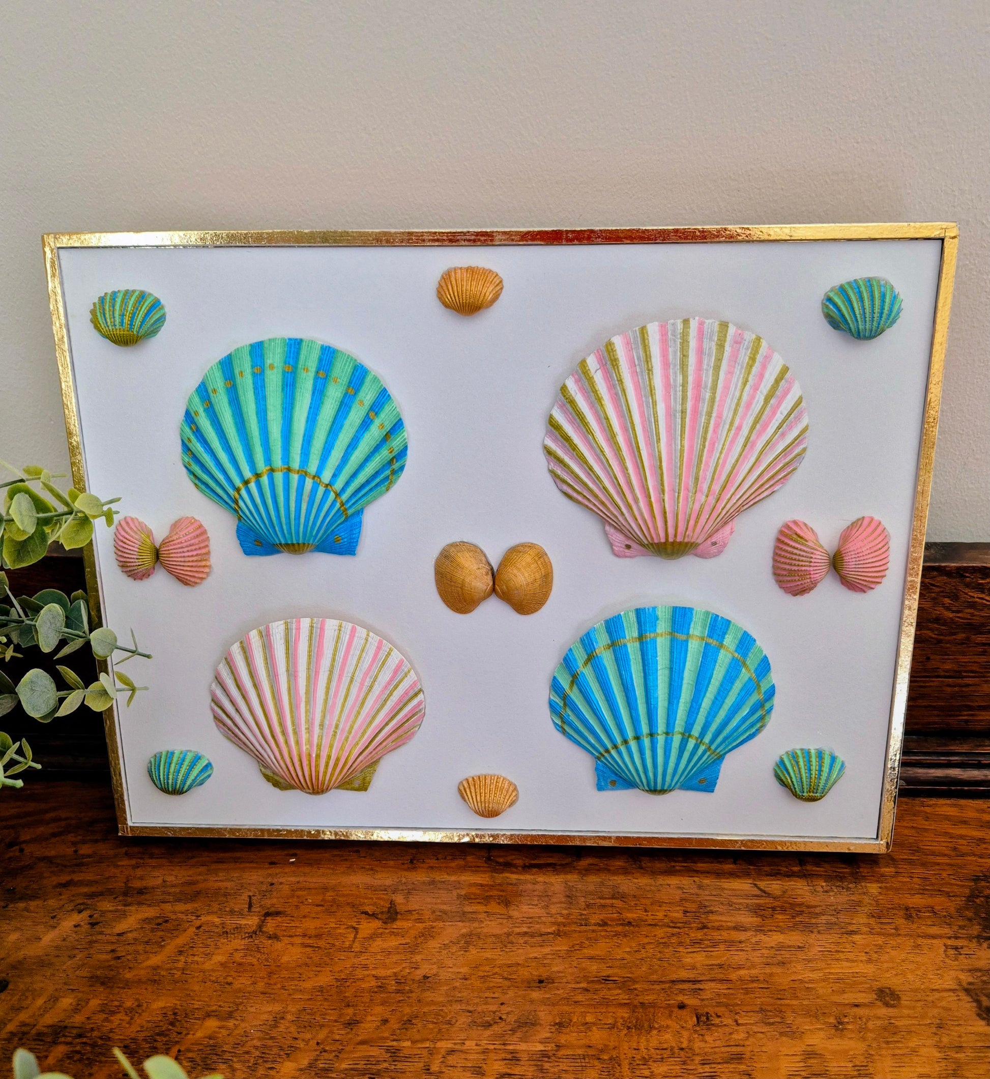 Decorative wall art with colorful shell designs on a white background, framed in gold.