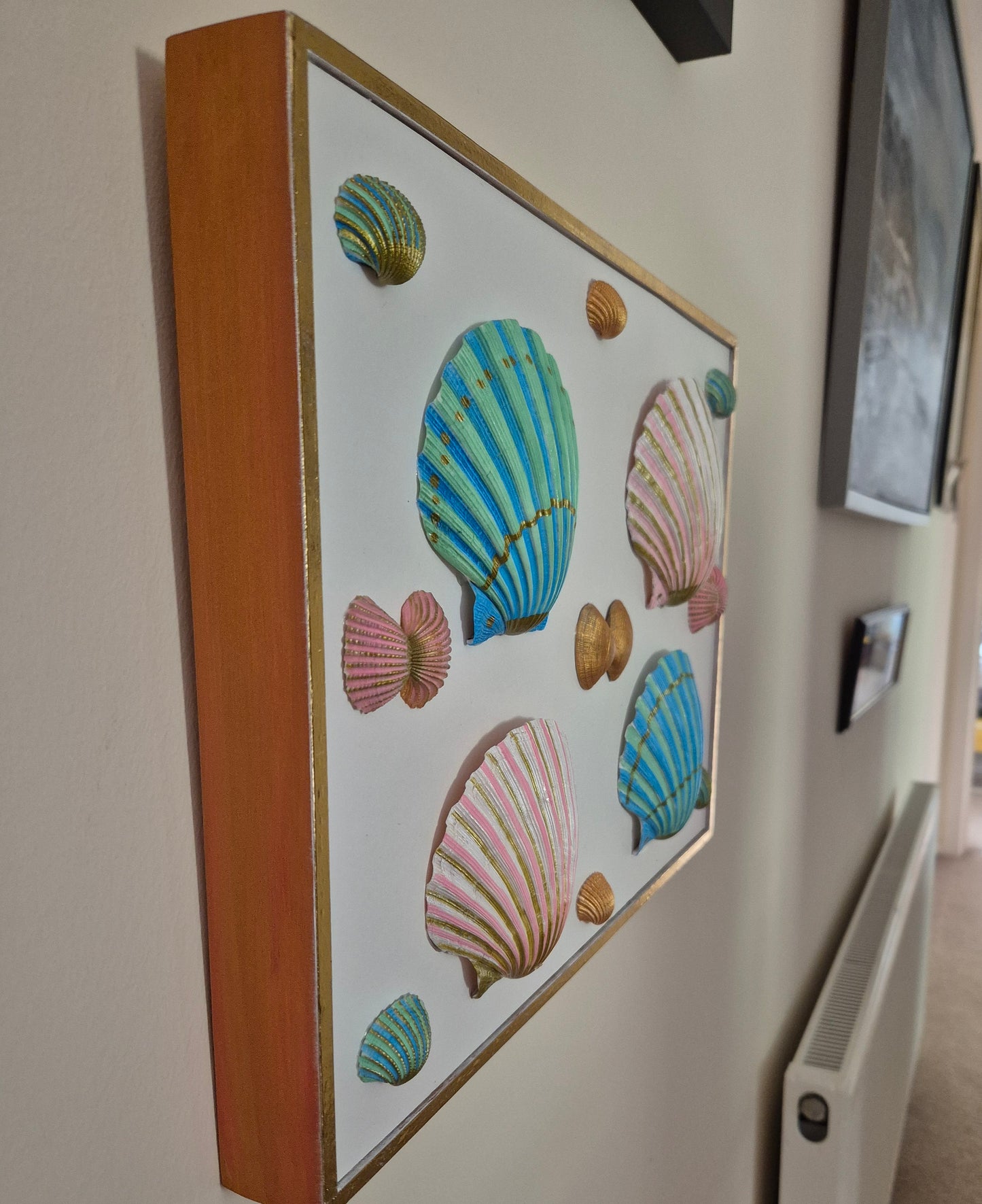 Framed artwork with colorful shell designs on a wall.